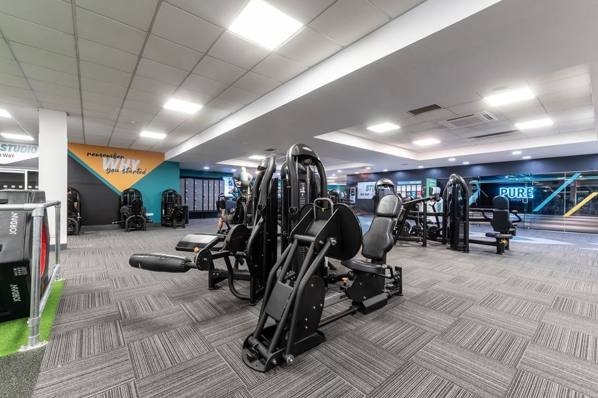 PureGym Woking: Resistance training machines, benches, weight racks, and rubberized floors in a gym space.