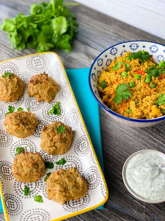 Baked falafel balls on a patterned tray, bowl of couscous with vegetables, and sauce bowl.