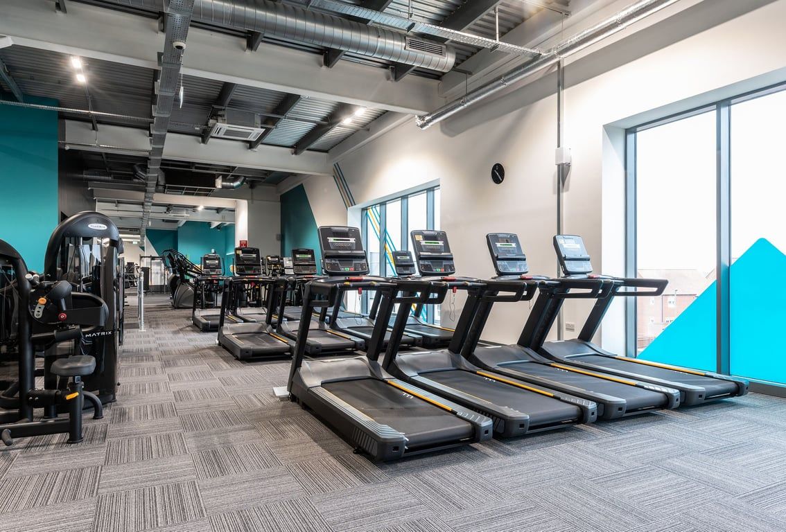 PureGym Bicester: Rows of treadmills, sleek design with turquoise accents and exposed ductwork.