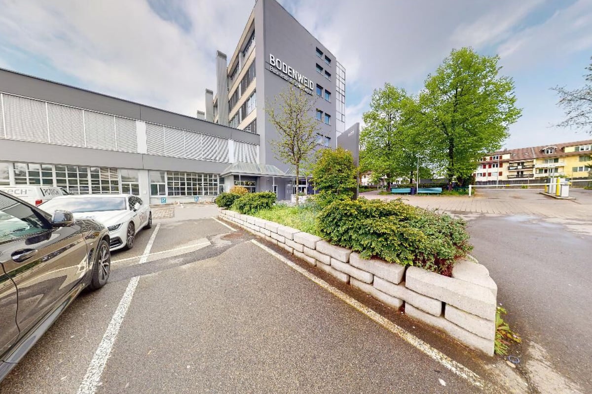 PureGym Bern Bümpliz: Extérieur d'un bâtiment de plusieurs étages avec des arbres et des voitures garées sur une surface pavée.