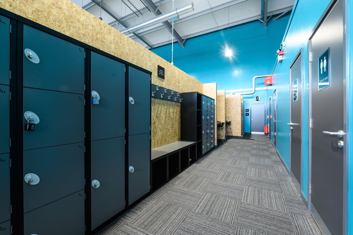 PureGym Maldon Blackwater Retail Park: Rows of lockers, benches, and tiled floors in a changing room area.
