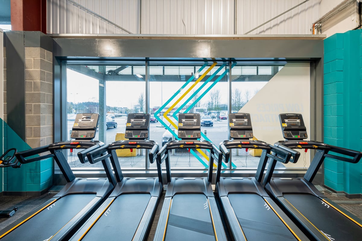 PureGym Elgin: Rows of treadmills facing large windows overlooking cityscape.