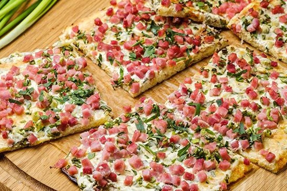 Fladenbrotscheiben mit gewürfeltem Schinken, Kräutern und cremiger weißer Sauce auf Holzbr