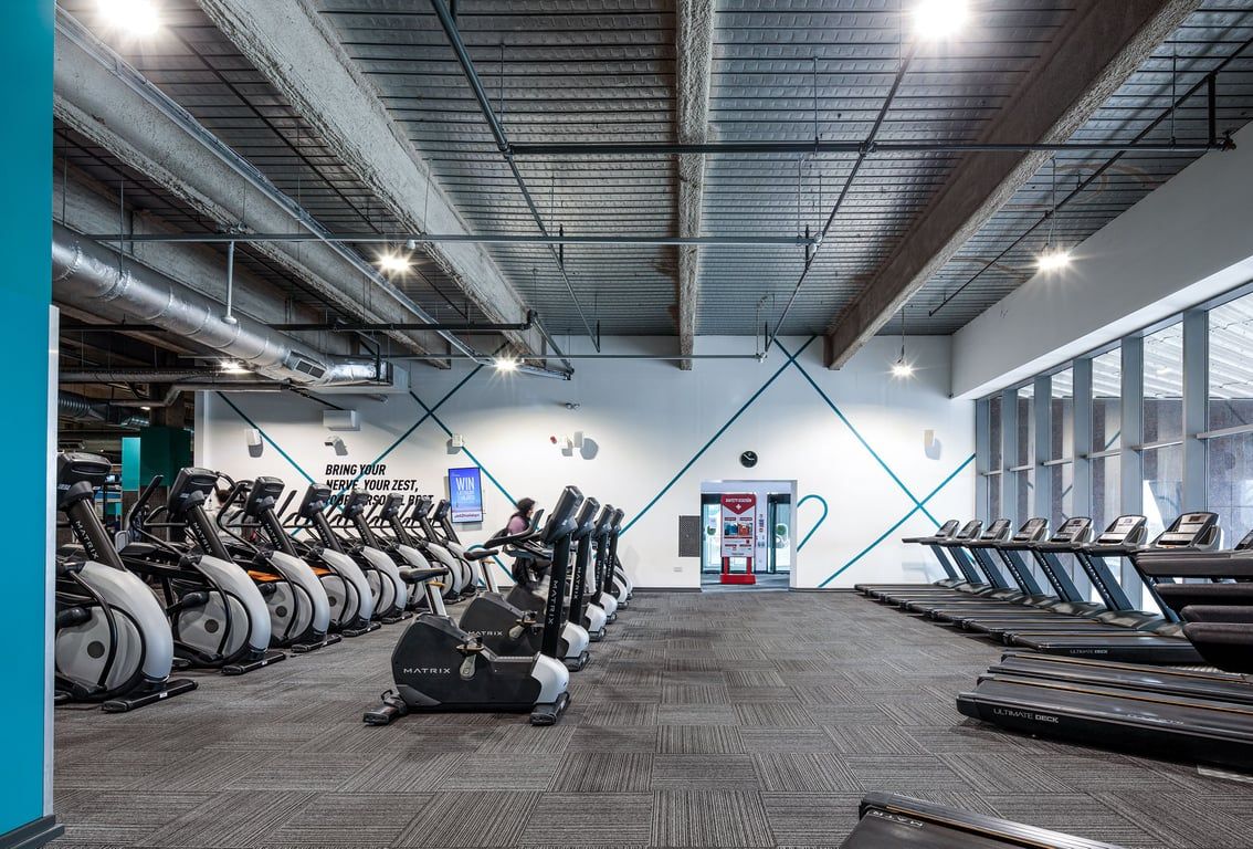 PureGym Cardiff Central: Rows of treadmills, exercise bikes, and weight benches in a gym with exposed ceiling beams.