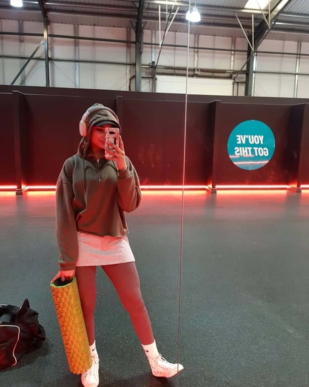 Woman in sportswear holding a foam roller taking a mirror selfie in a gym room