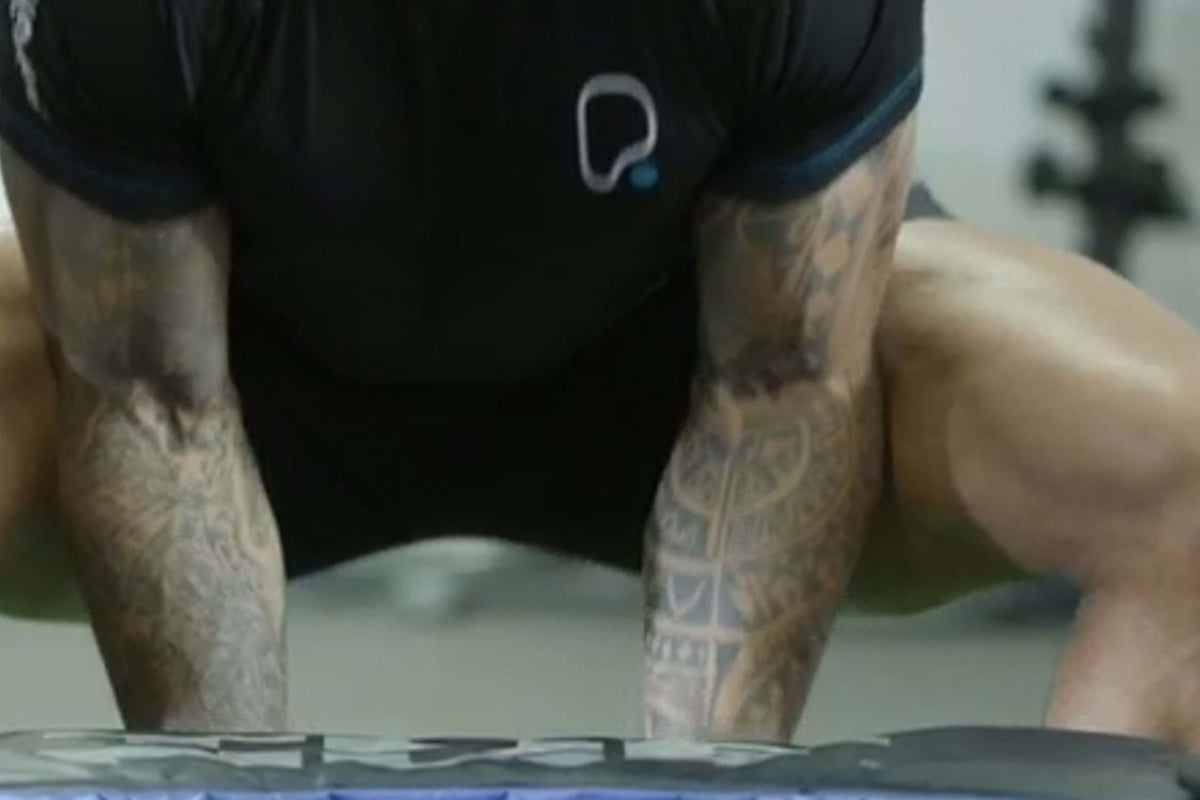 Tattooed arms and muscular legs of a person in a black shirt doing a workout.