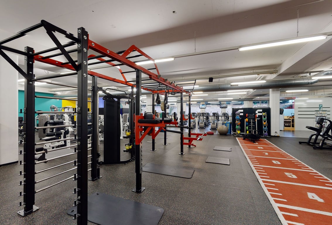 PureGym Dübendorf: Krafttrainingsgerät, Hantelständer, gummierter Boden und Spiegel.