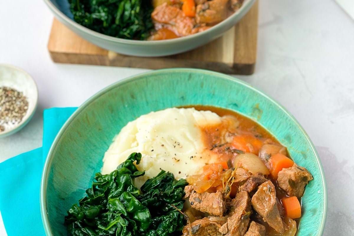 Mashed potatoes, cooked kale, and beef stew with carrots and onions in bowls