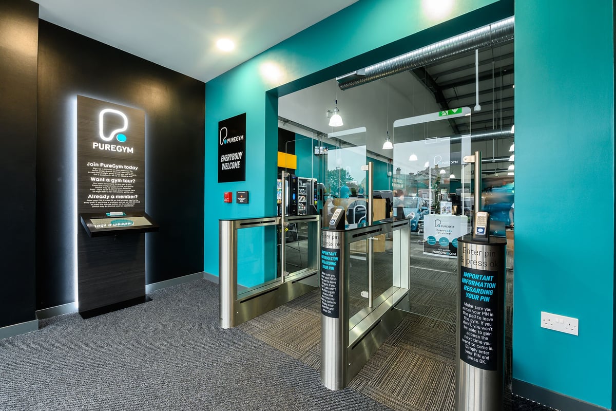 PureGym Bromsgrove Retail Park: Reception area with self-service kiosks, teal branding, and glass partitions.