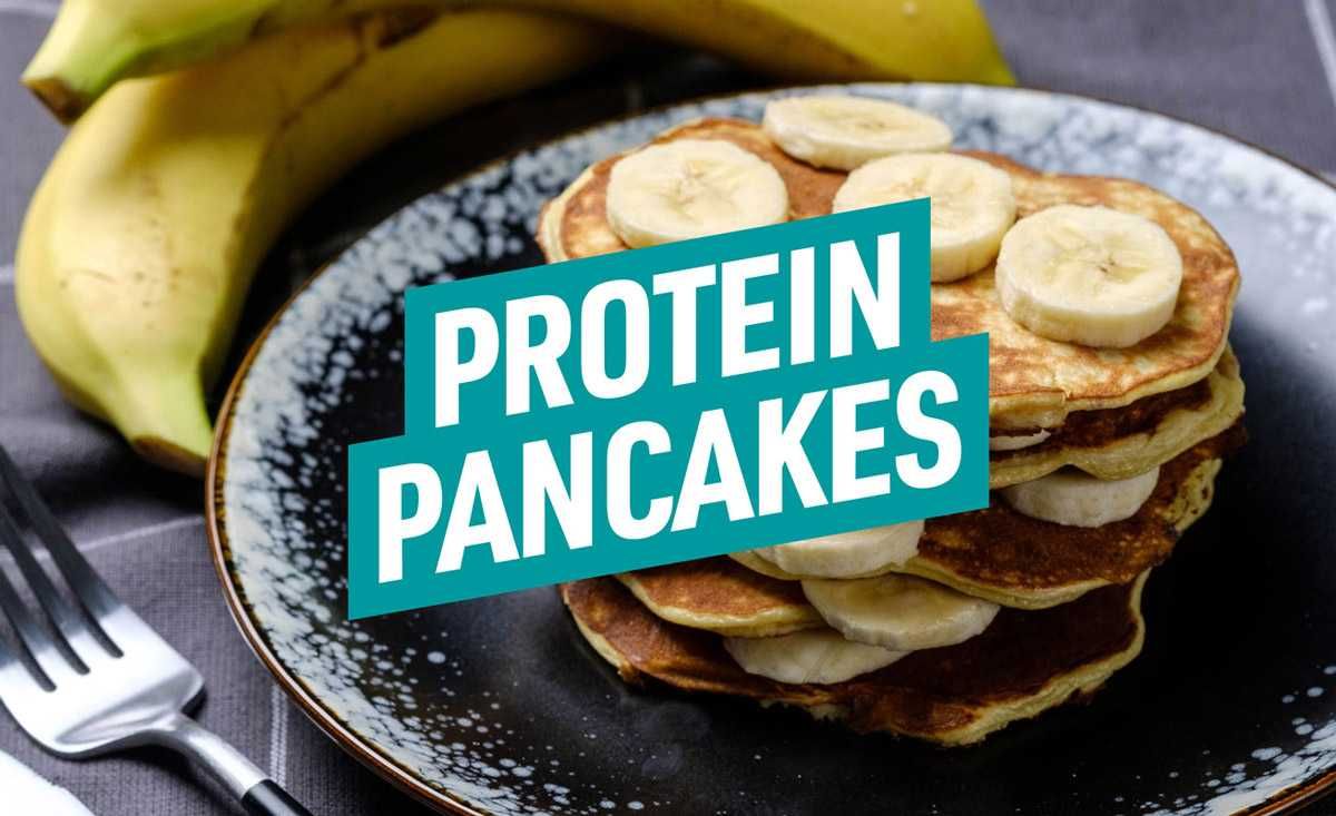 Stapel Pfannkuchen mit Bananenscheiben auf schwarzem Teller, daneben Banane und Gabel