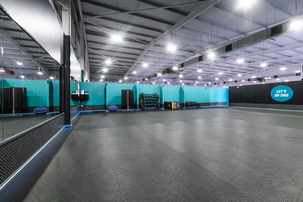 PureGym Widnes: Teal-coloured gym studio with weightlifting platforms, squat racks, and rubberized flooring.
