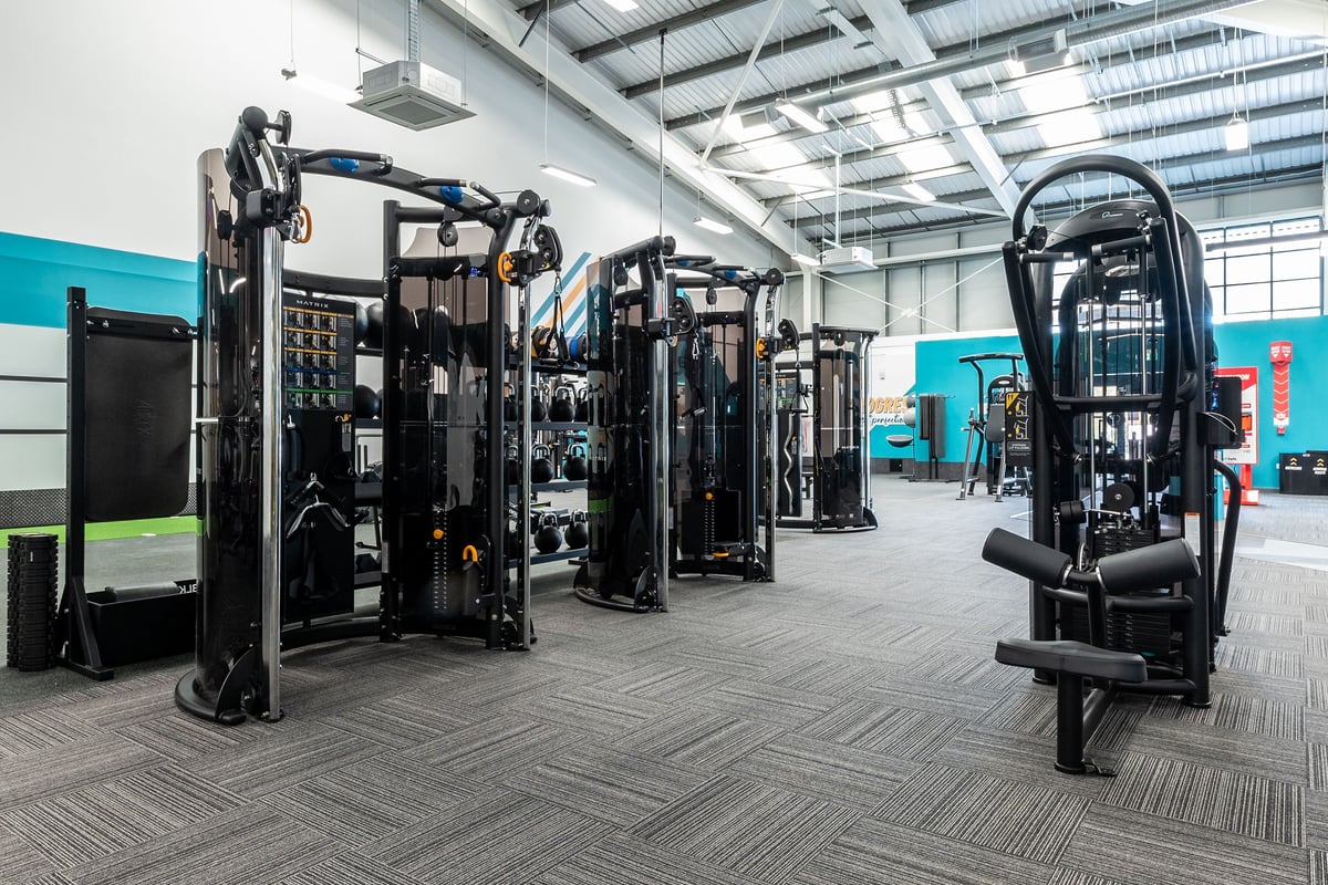 PureGym Kettering: Rows of resistance machines, cable crossovers, and weight racks on rubberized flooring.