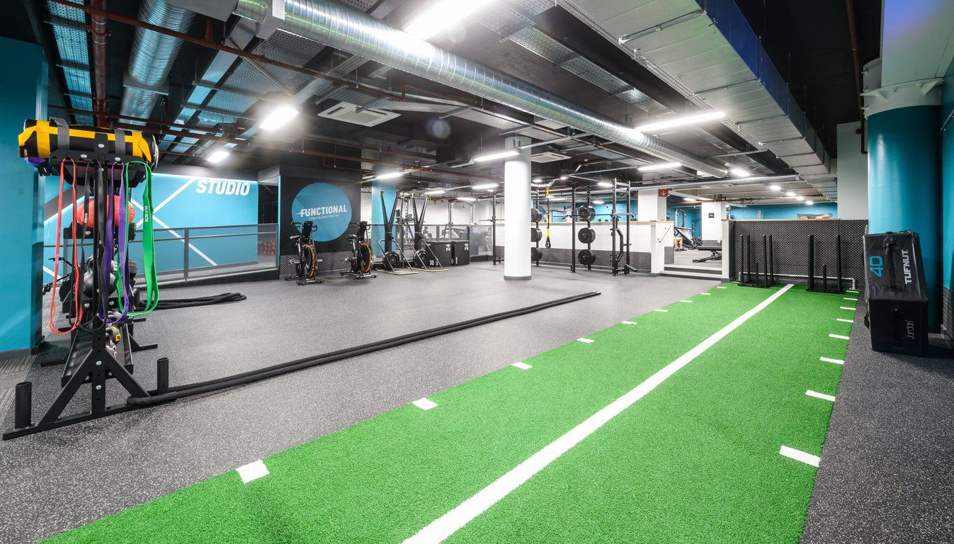 PureGym London East India Dock: Functional training area, green turf, resistance machines, free weights, and studio signage.