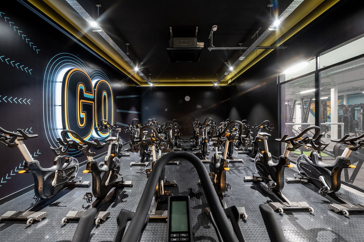 PureGym Yeovil Houndstone Retail Park: Rows of stationary bikes, neon lighting in a dark studio setting.