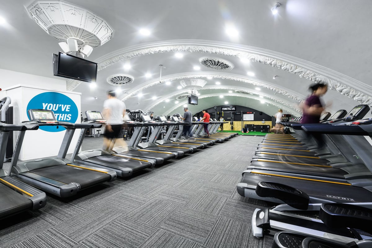PureGym London Wandsworth: Rows of treadmills and illuminated ceiling arches in a modern gym setting.