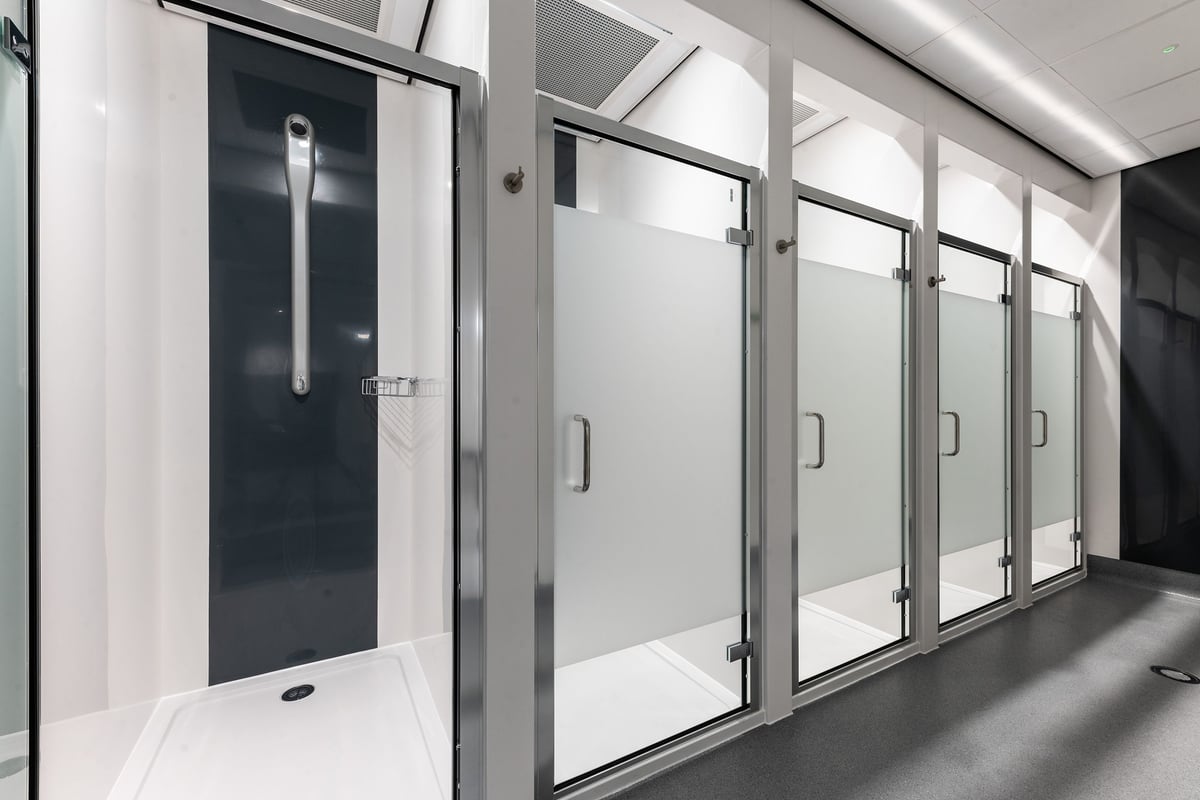 PureGym Solihull Sears Retail Park: Rows of frosted glass shower stalls or changing cubicles with door handles.