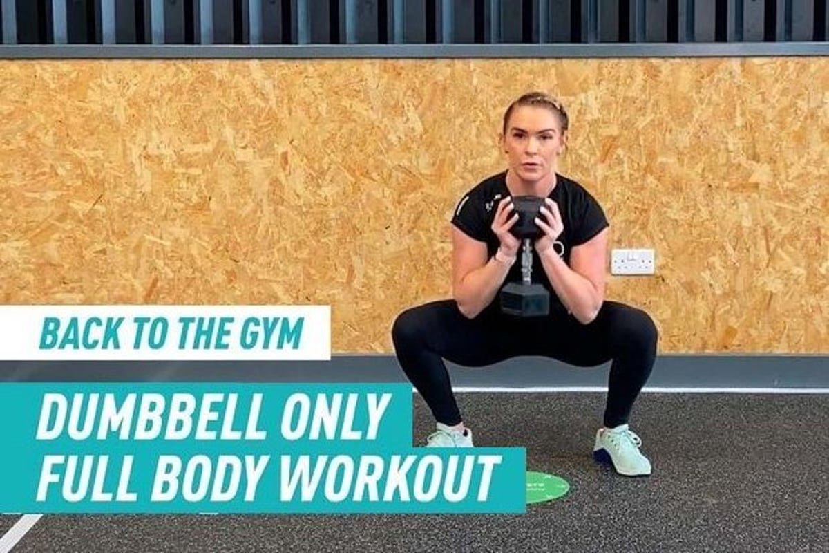 Woman in black workout clothes holding dumbbell in a squat position on gym floor