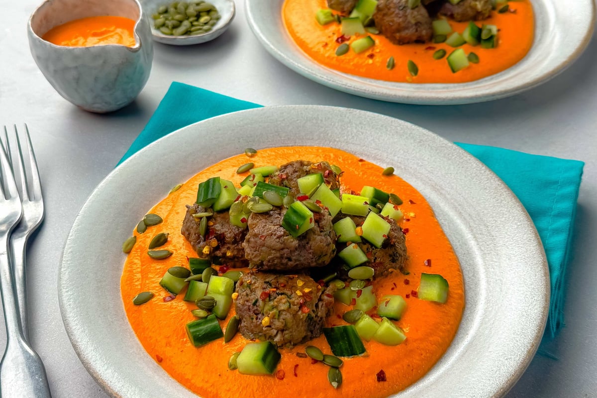 Meatballs on orange sauce topped with diced cucumber and pumpkin seeds on white plates.