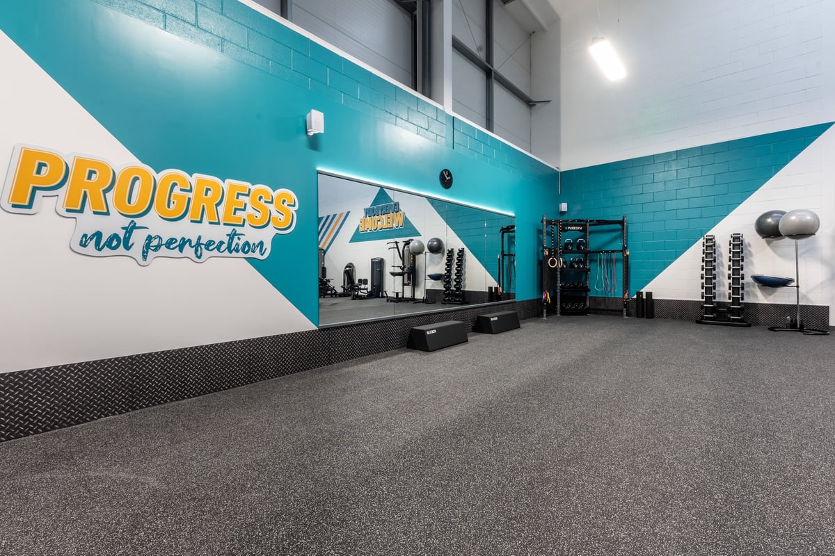 PureGym Port Talbot: Loading bay with "Progress not perfection" mural, trucks, and industrial equipment.