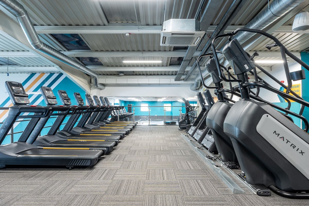 PureGym Brierley Hill: Rows of treadmills and other cardio machines in a brightly lit gym interior.