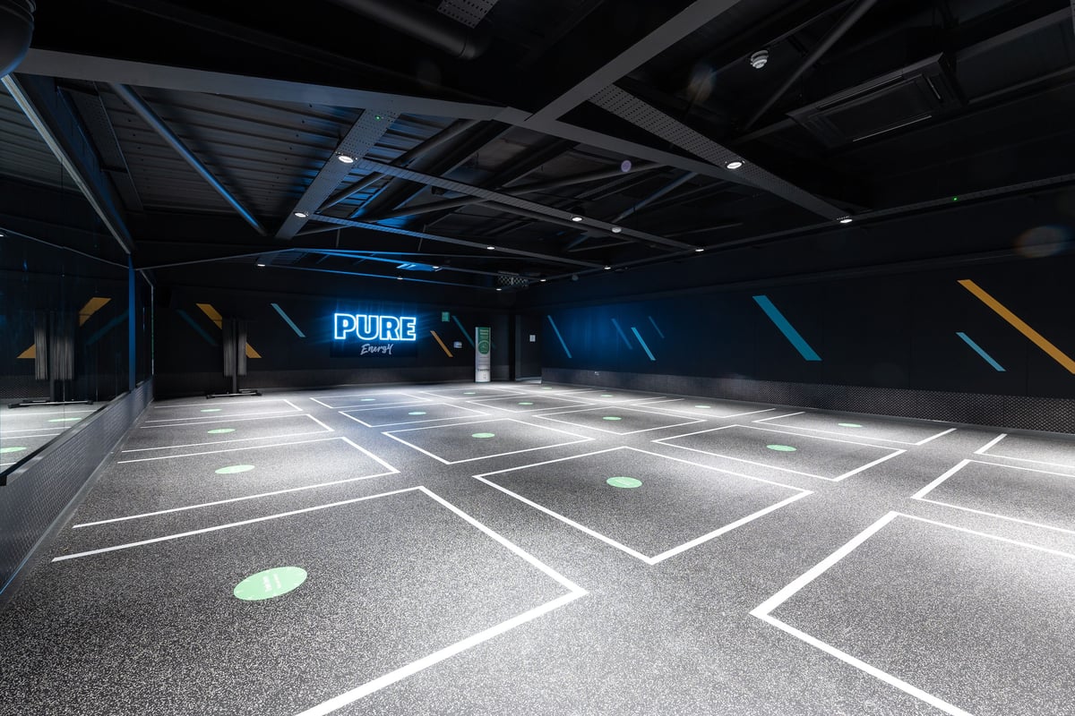 PureGym Colchester Retail Park: Modern gym studio with blue neon lights, rubberized flooring, and futuristic interior.