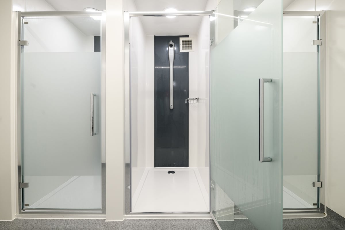 PureGym London Whitechapel: Glass-enclosed shower stall areas with sliding doors and grab bars.