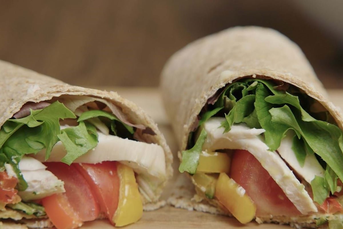Two halves of a wrap filled with lettuce, tomato, cheese, and yellow pepper on a wooden board