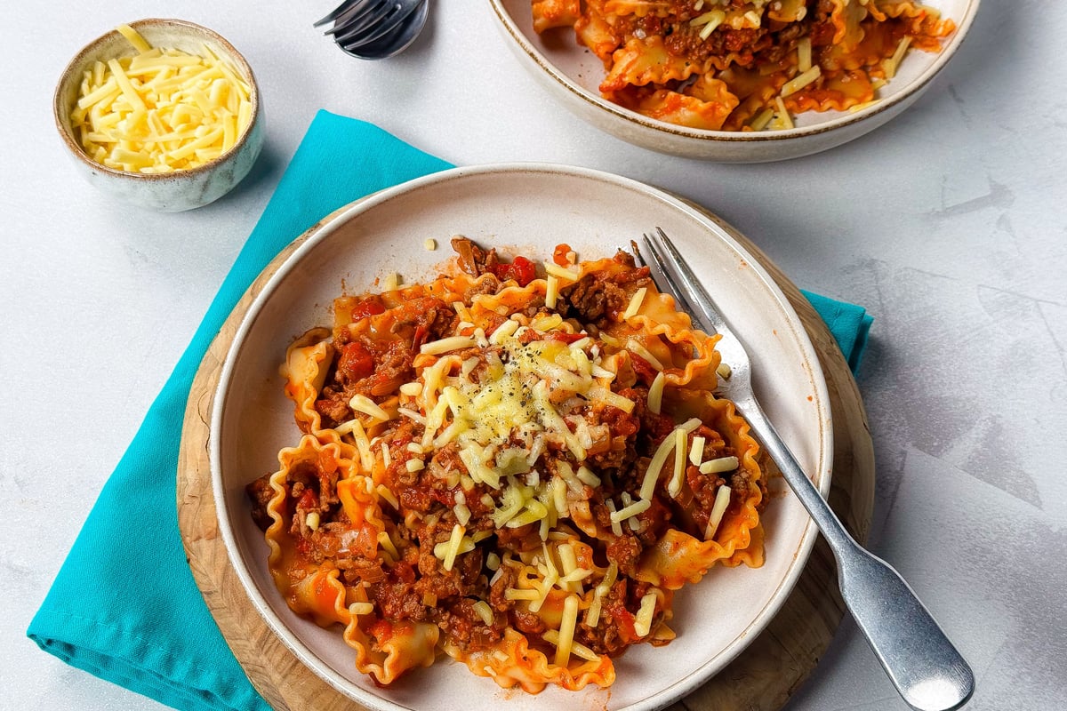 Two plates of pasta with meat sauce and grated cheese, fork on one plate, bowl of cheese
