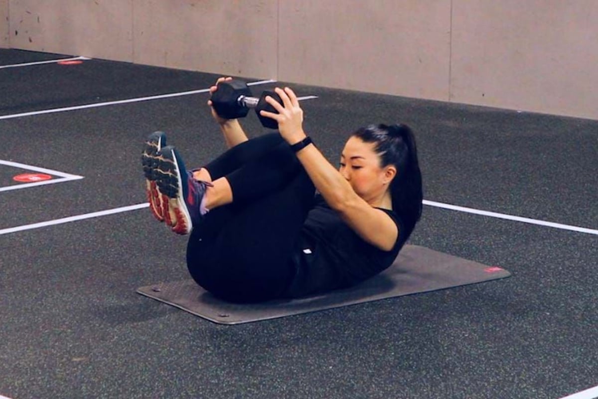 Woman in black workout clothes holding dumbbells while doing abdominal exercise on mat