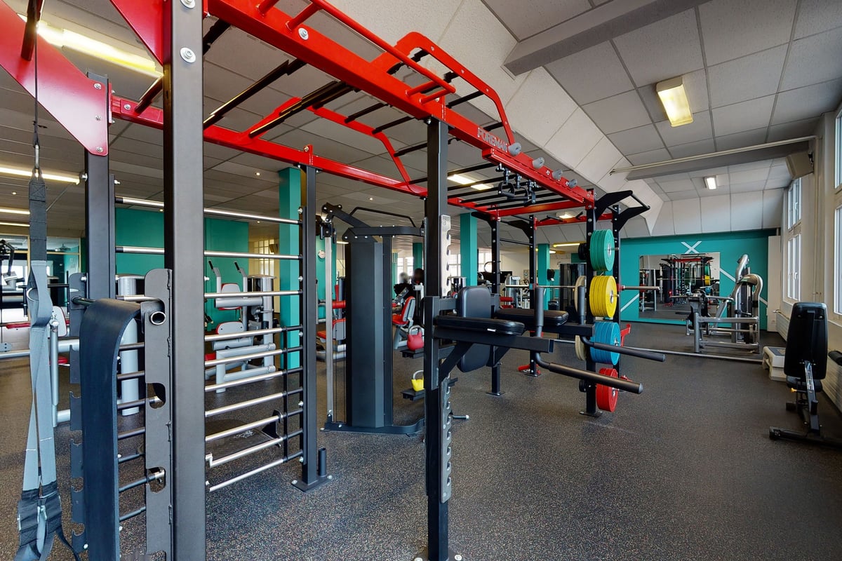 PureGym Rorschach: Salle de sport avec appareils de traction, haltères, bancs et sols caoutchoutés dans une palette de couleurs rouge et bleu sarcelle.