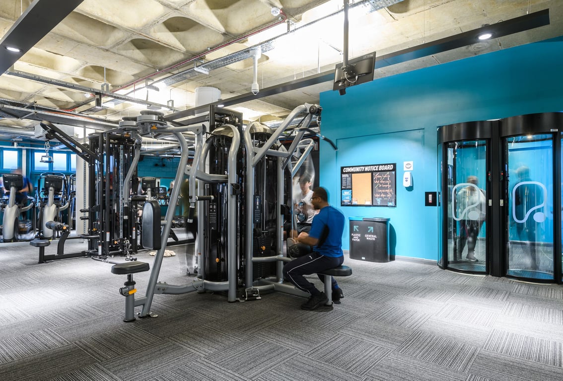 PureGym London Farringdon: Gym floor with strength training machines, a blue wall, and rubberised flooring.