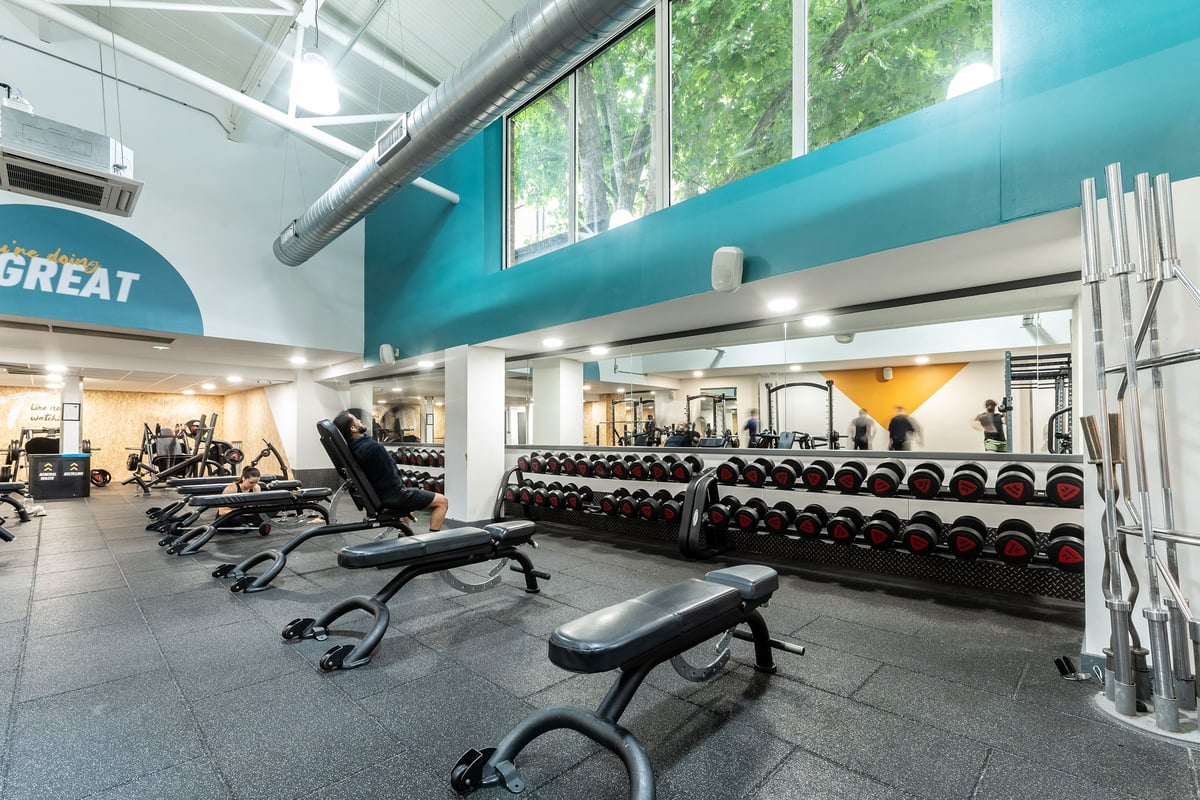 PureGym London Bayswater: Weight benches, dumbbell racks, resistance machines, and floor mats in a brightly lit gym area.