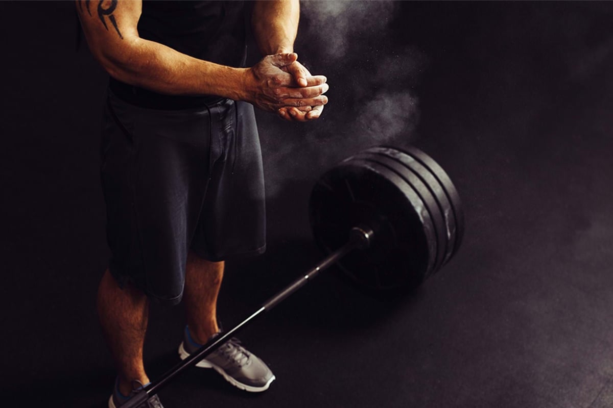 Man clapping chalked hands near a heavily weighted barbell on the floor