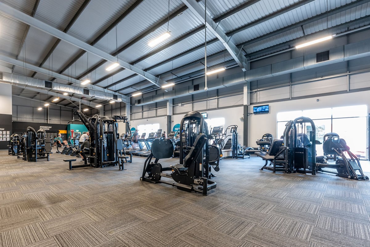 PureGym Widnes: Rows of strength machines, cable crossovers, benches, and rubberized flooring in a well-lit gym space.