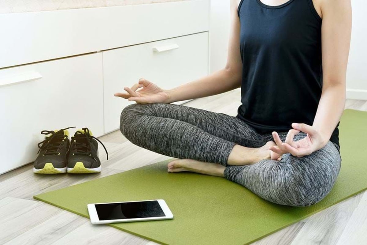 Person sitting cross-legged on a green yoga mat meditating with shoes and tablet nearby