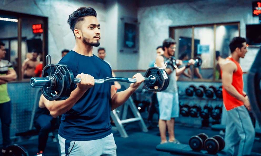 Young men lifting weights in a gym with mirrors and dumbbells in the background