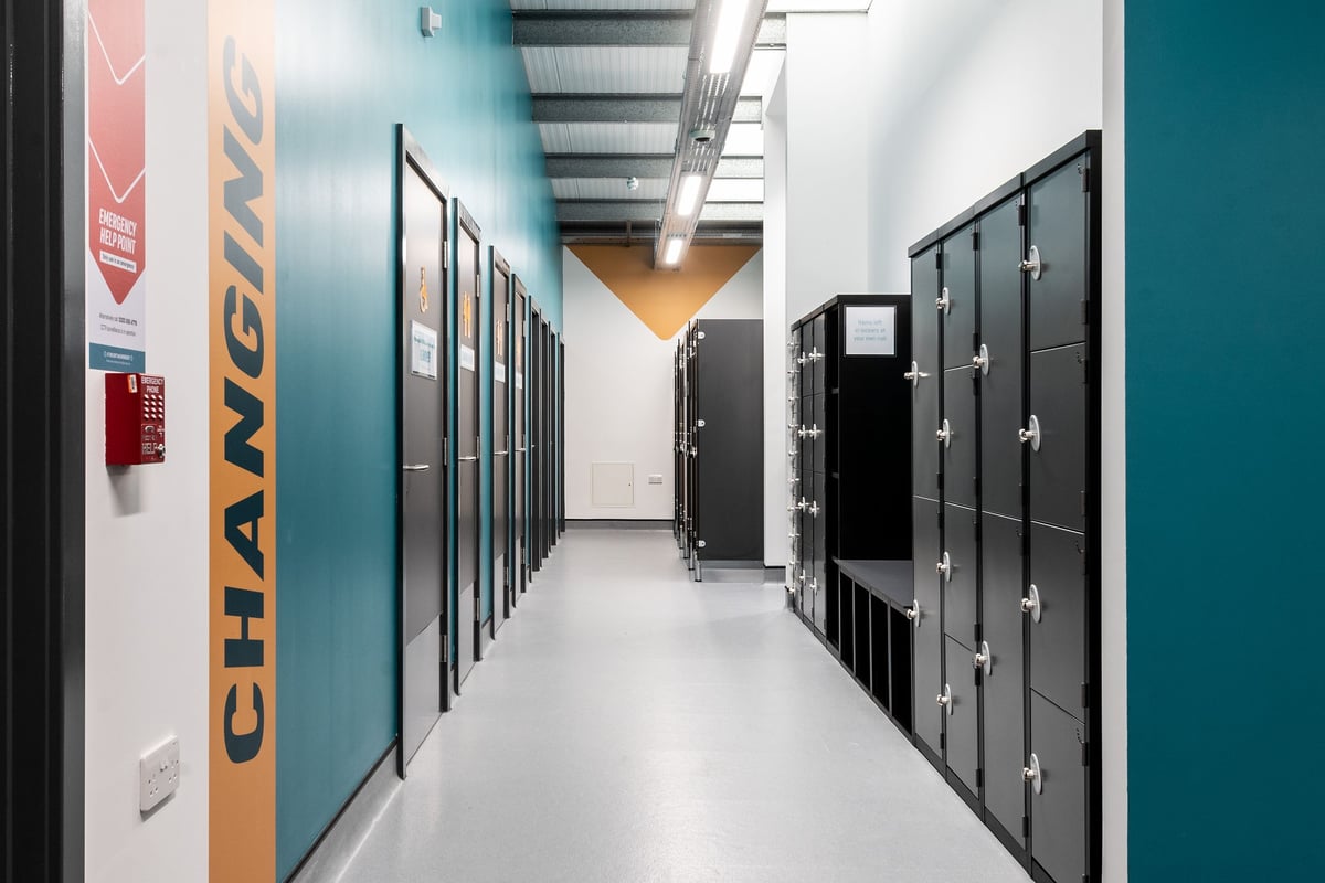 PureGym Ormskirk: Rows of black lockers lining a corridor with tiled flooring and branded wall signage.