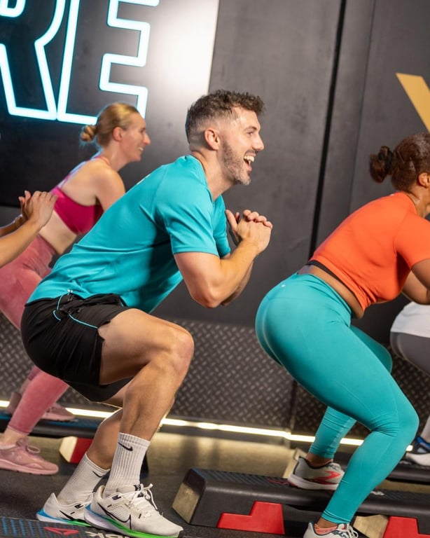 Energische Gruppe trainiert zusammen in einem modernen PureGym Studio mit Neonbeleuchtung und motivierender Atmosphäre