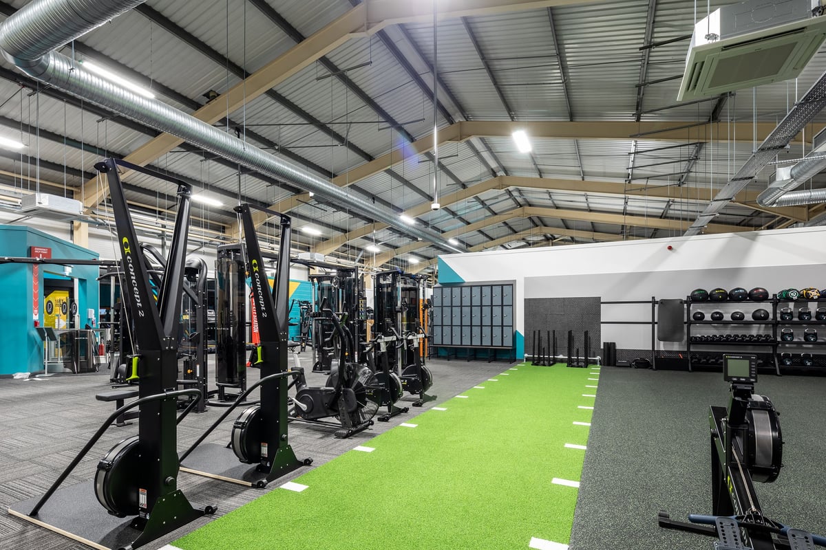 PureGym Neath: Gym studio with weight racks, resistance machines, turf area, free weights, and rubberized flooring.