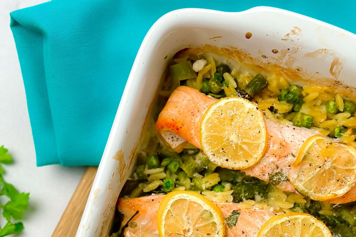 Baked salmon fillets with lemon slices on orzo rice with peas and vegetables
