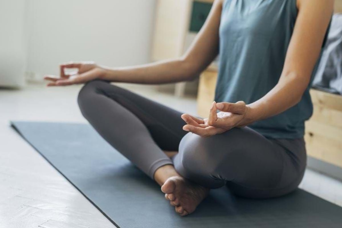 Person sitting cross-legged on a yoga mat with hands in meditation pose.