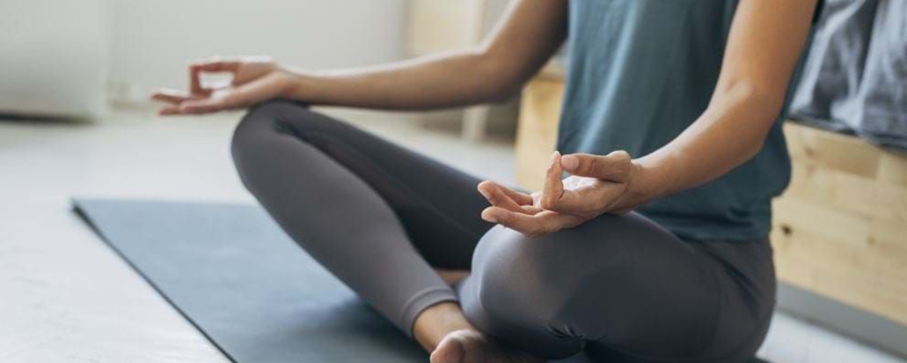 Person sitting cross-legged on a yoga mat with hands in meditation pose.