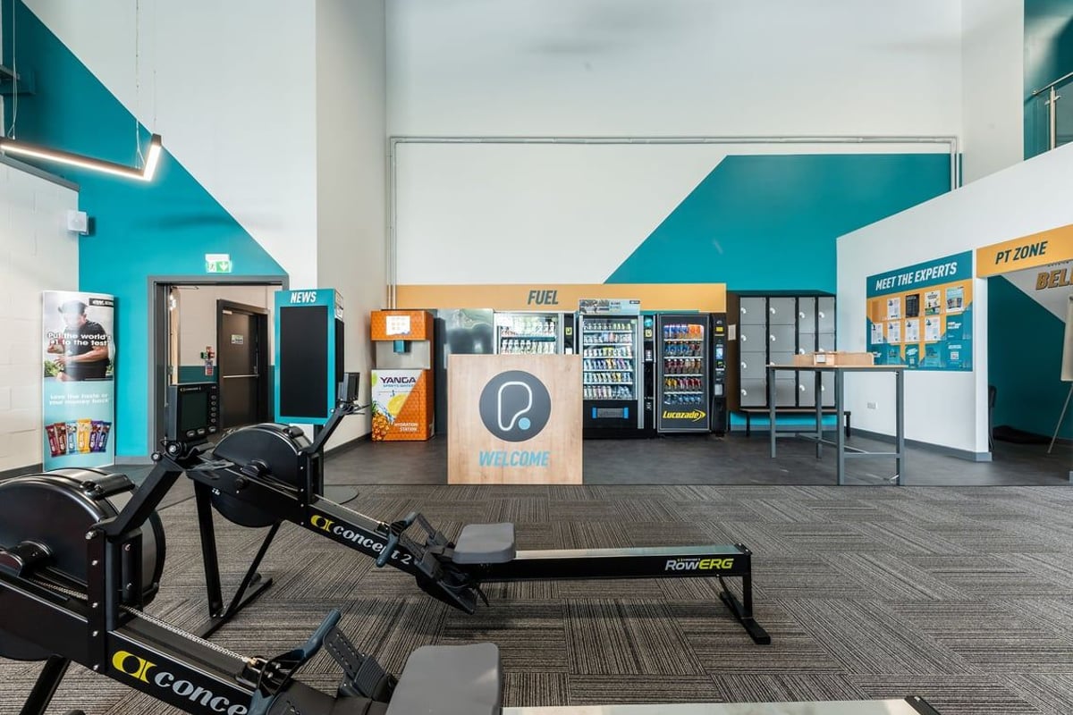 PureGym Tamworth: Rowing machine, vending machines, seating area in teal and white decor.
