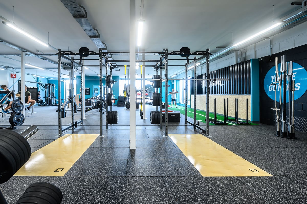 PureGym Barnstaple: Squat racks, weight plates, rubberized flooring, and mirrored walls inside a brightly lit gym studio.