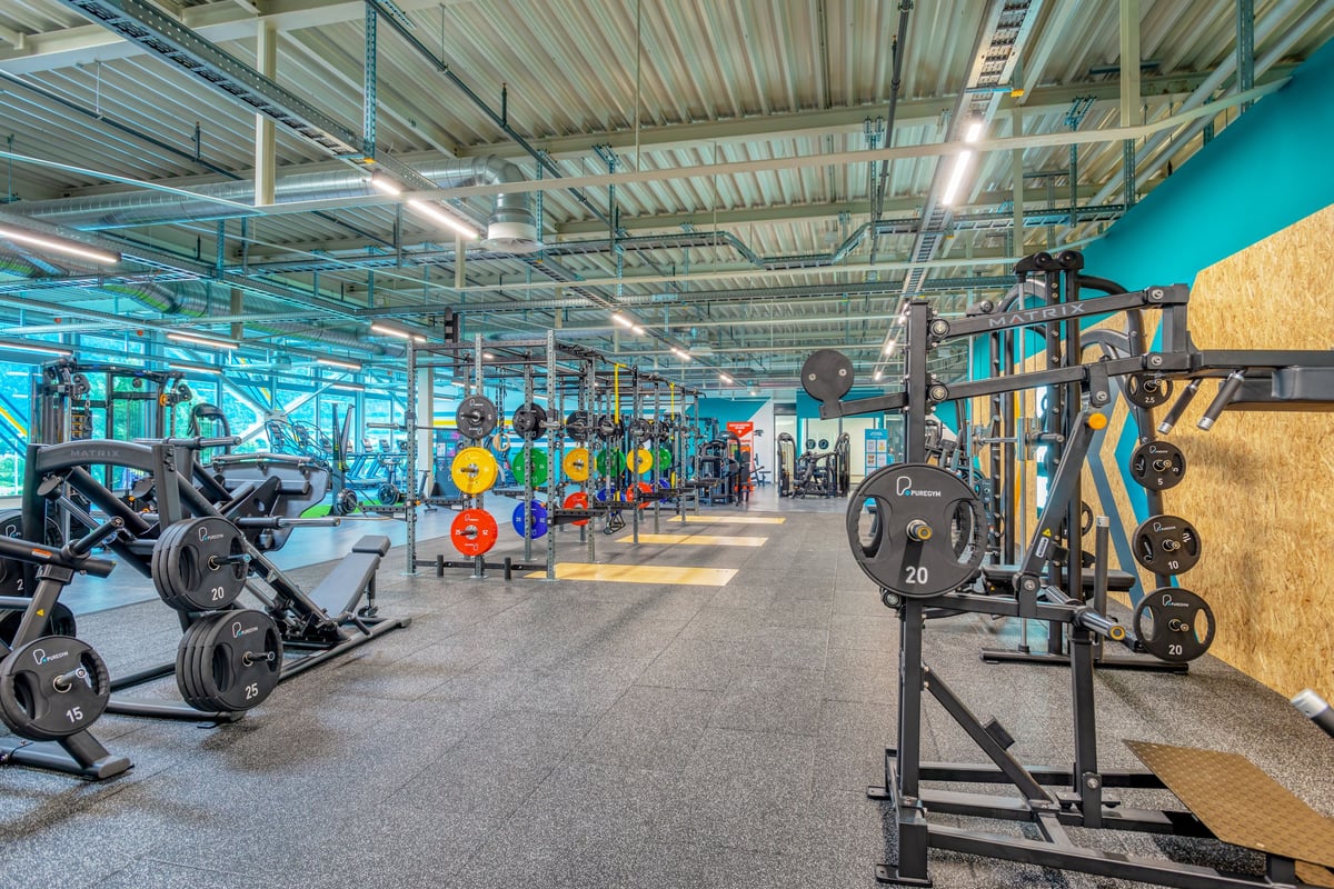 PureGym Martigny: Innenausstattung des Fitnessraums mit Hockstützen, Hantelscheiben, Bänken, gummierten Böden und verspiegelten Wänden.