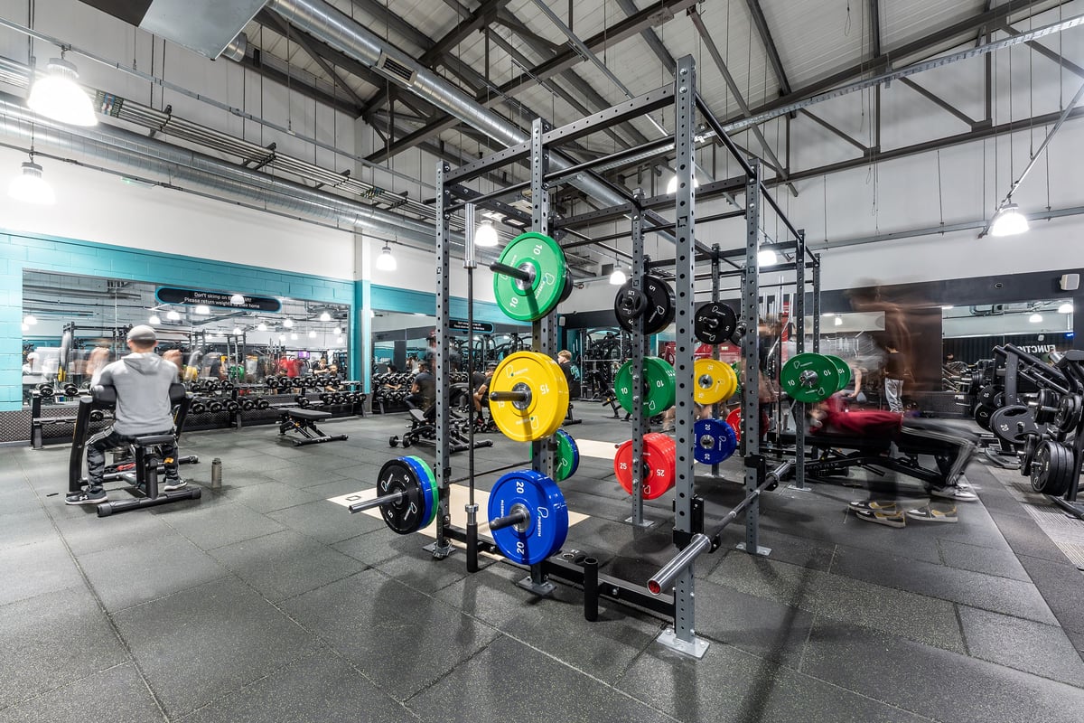 PureGym Wolverhampton Bentley Bridge: Gym setting with weight racks, colourful plates, benches, and industrial ceiling.