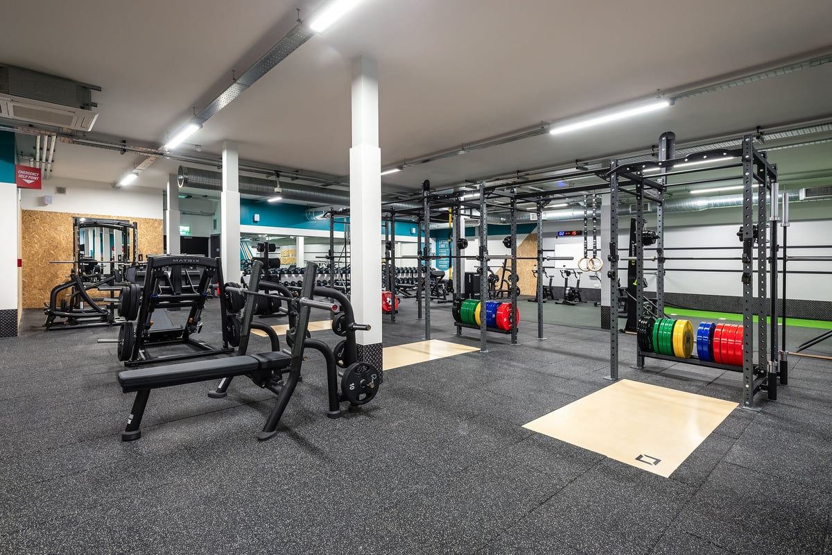 PureGym Llantrisant: Weight racks, benches, free weights, rubberized flooring in a gym space with bright lighting.