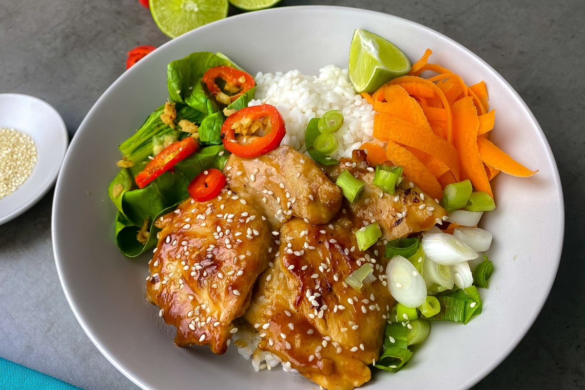 Glazed chicken with sesame seeds on white rice with vegetables and lime wedge