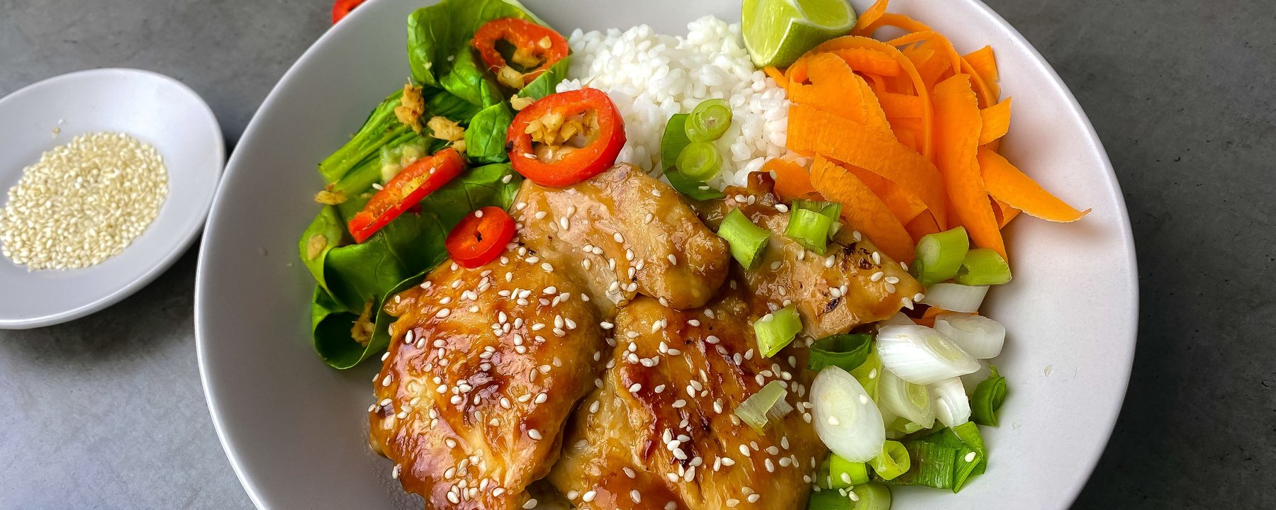 Glazed chicken with sesame seeds on white rice with vegetables and lime wedge