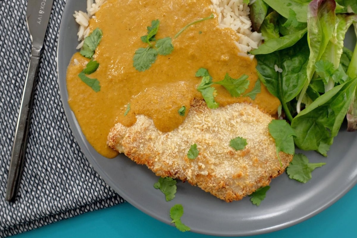Breaded chicken with curry sauce, white rice and salad leaves on grey plate